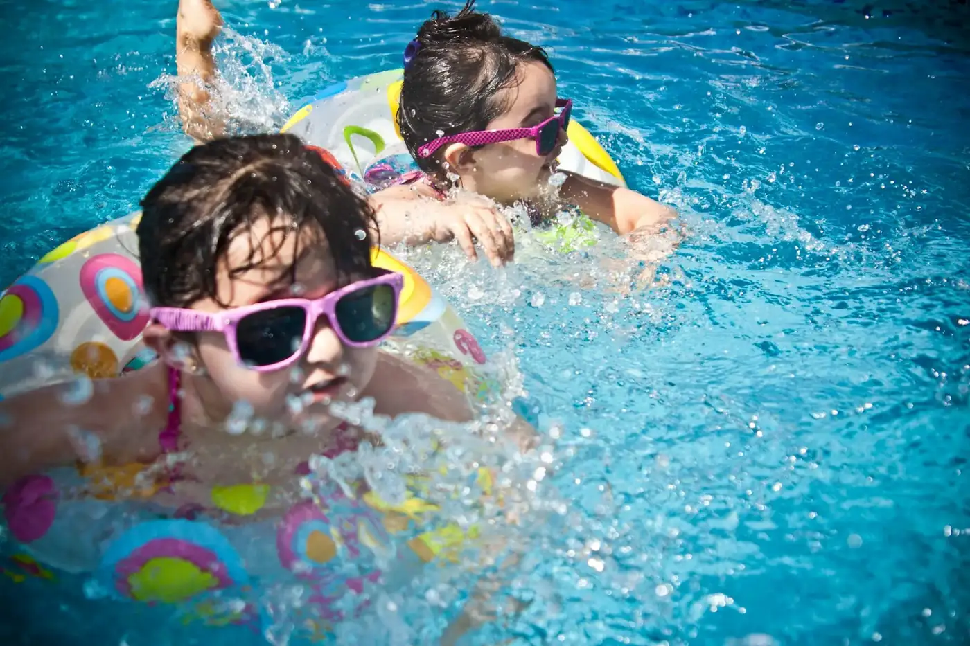 Zwei Kinder mit Schwimmreifen und Sonnenbrillen haben Spaß im Pool
